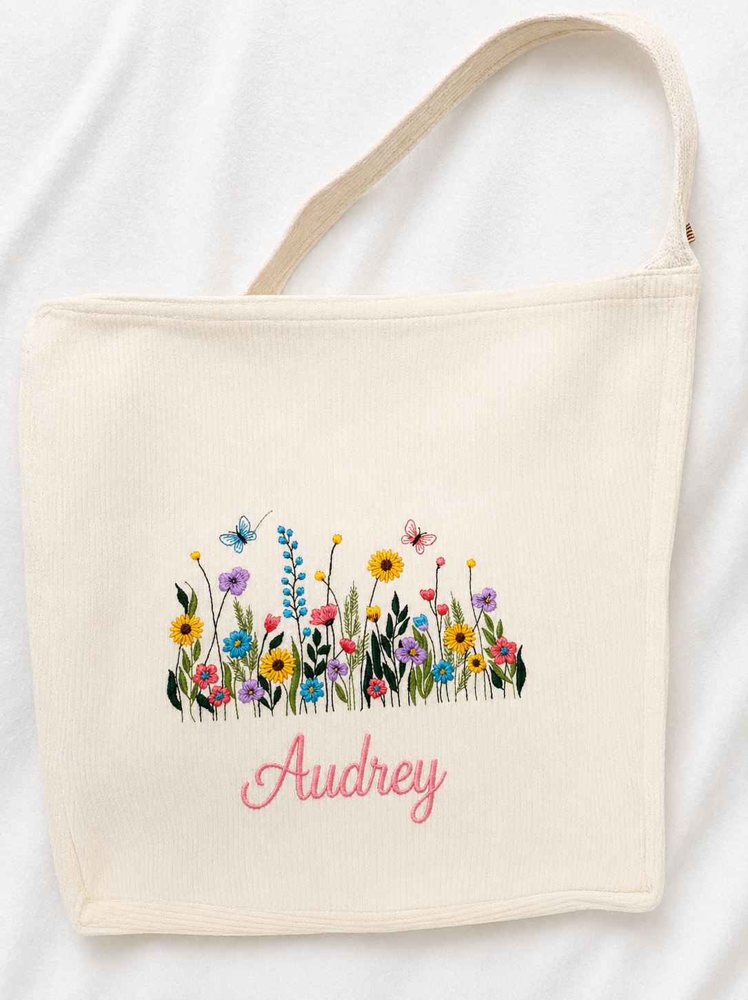 A soft corduroy tote featuring delicate wildflower embroidery and your custom name in a thick, elegant script. Durable, stylish, and perfect for everyday use or gifting.