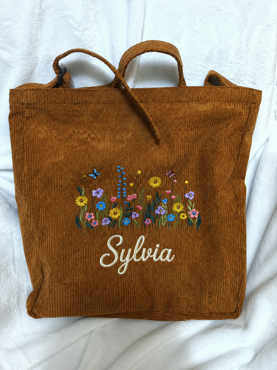 A soft corduroy tote featuring delicate wildflower embroidery and your custom name in a thick, elegant script. Durable, stylish, and perfect for everyday use or gifting.